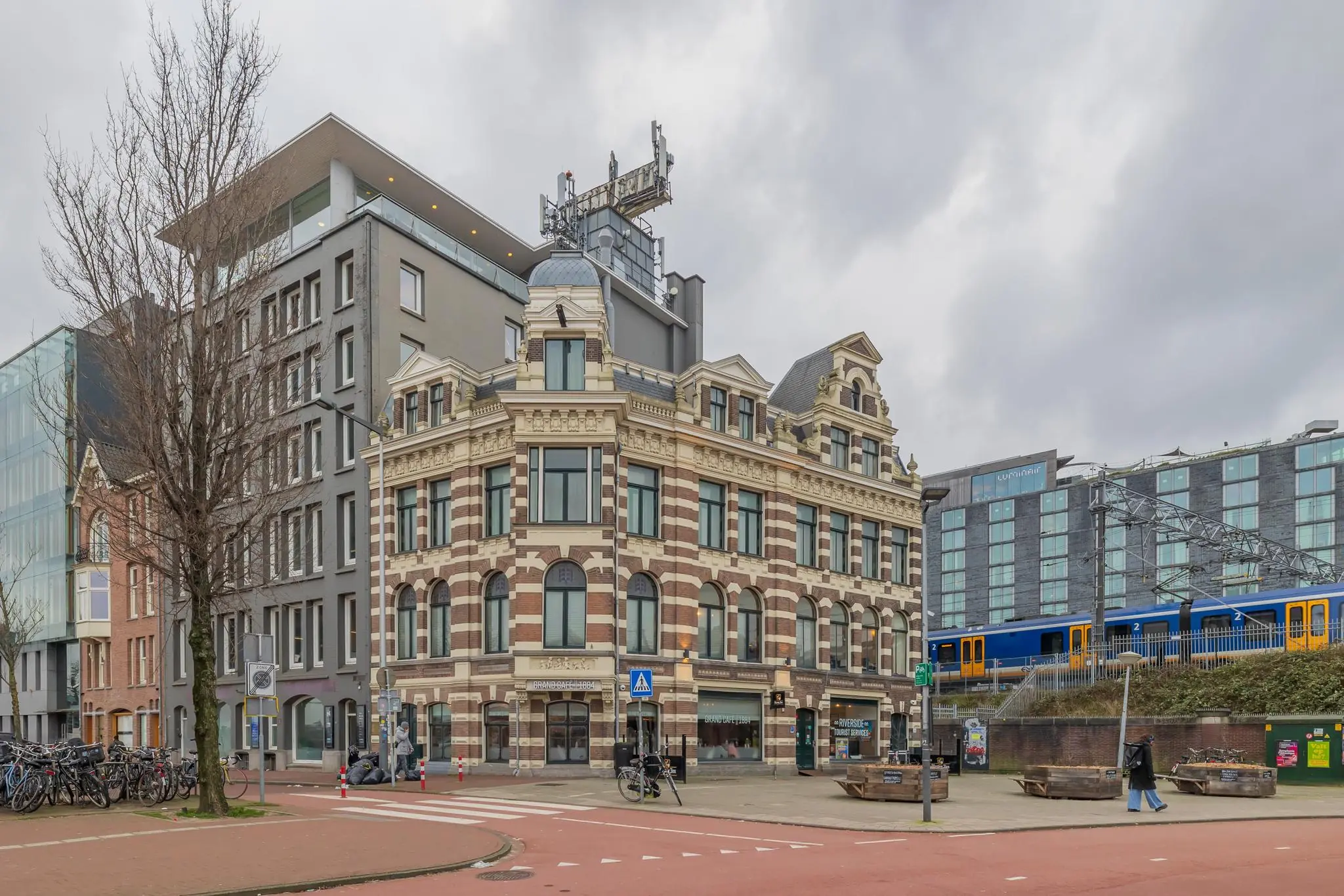 Historisch pand aan de De Ruijterkade in Amsterdam met een passerende trein op de achtergrond.